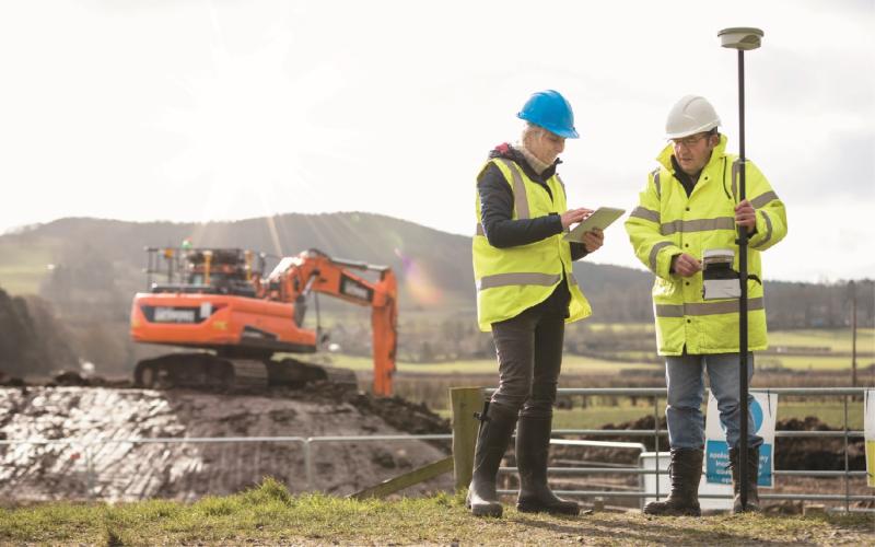 worksite with two people in high vis jackets and a digger