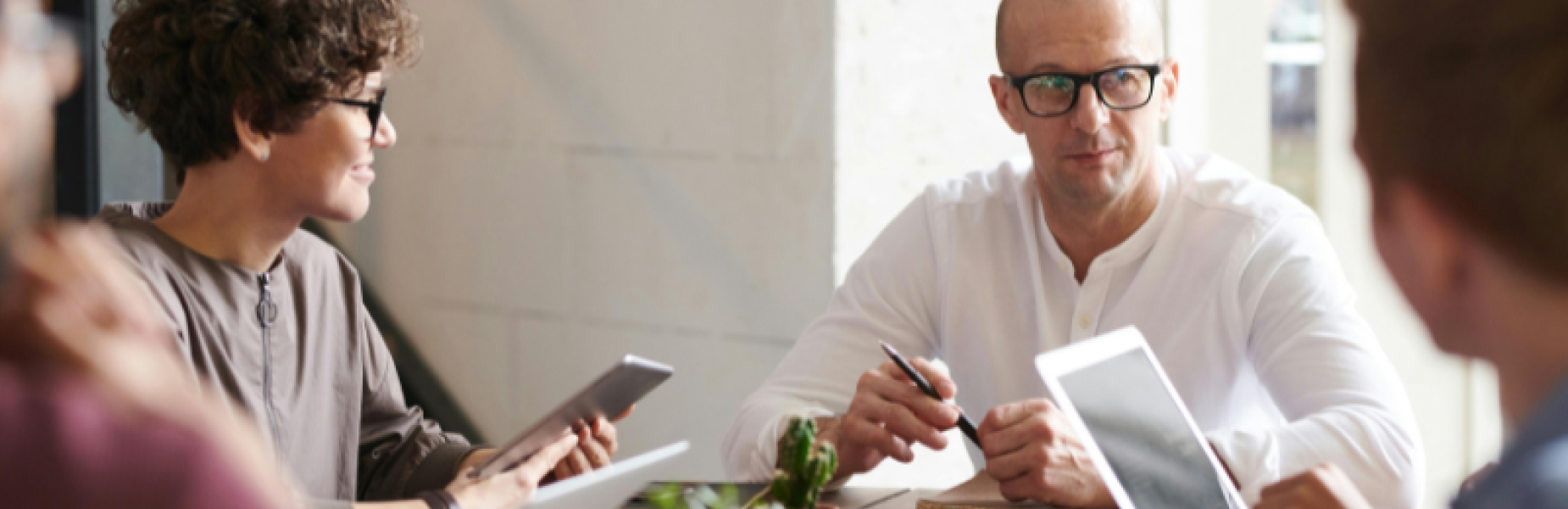 Group of people sitting around a wooden table in a modern office setting, engaged in a meeting.