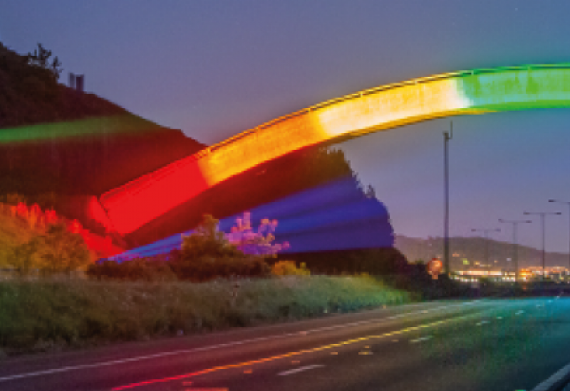 Photograph of a bridge lit up with neon rainbow lights