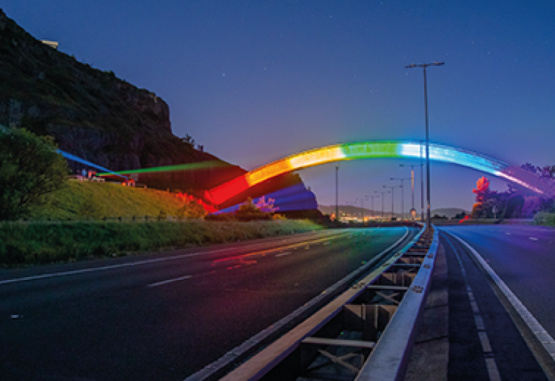Photograph of a bridge lit up with neon rainbow lights
