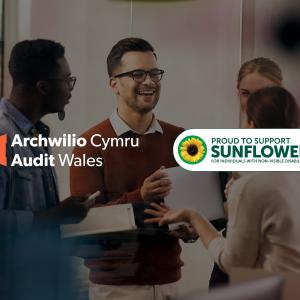 The image shows a group of four people standing together and having a discussion.There are two logos in the image: one on the left side that reads "Archwilio Cymru Audit Wales" with an orange triangular logo, and another on the right side that reads "PROUD TO SUPPORT SUNFLOWER FOR INDIVIDUALS WITH HIDDEN VISIBLE DISABILITIES" with a sunflower icon.